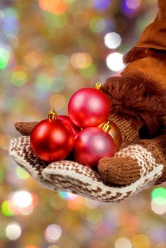 Hands dressed in mittens hold Christmas balls on an abstract color background