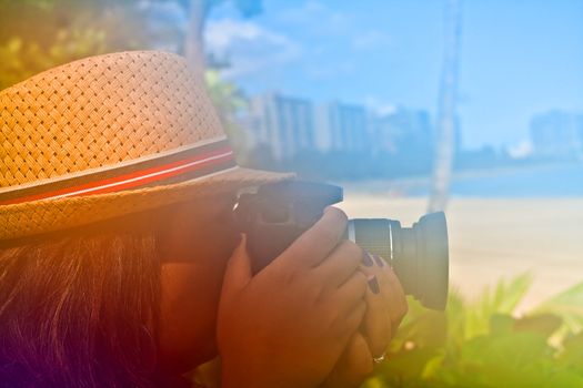 Woman photographer shooting with her digital camera outdoors in a tropical area with abstract color glow.