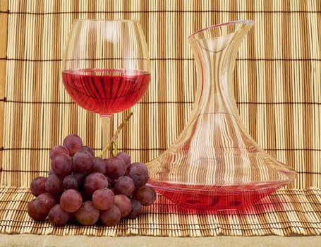 Still life with decanter, goblet and grapes on mat background