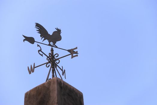 Wind vane in a form of a rooster on the top of a roof. 