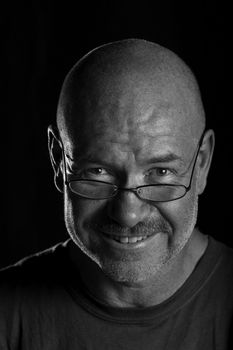 Dramatically lit head shot of older man looking over his glasses and smiling