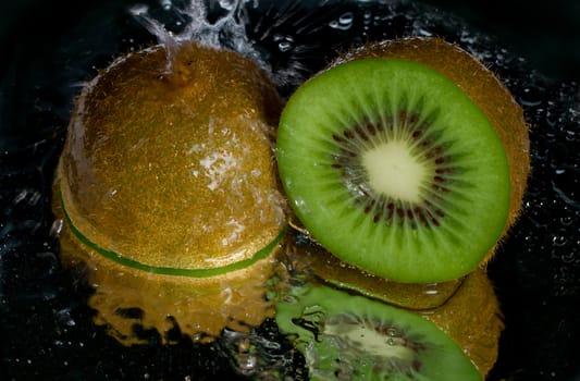 kiwi dousing with water, with reflection, on black background