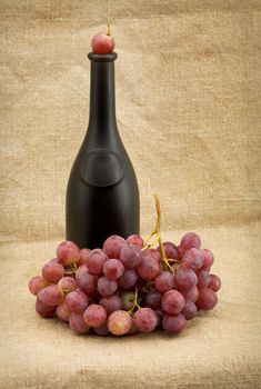 Dark bottle and red grapes bunch on background the canvas