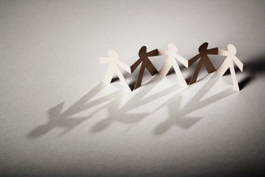 Line of cutout paper dolls throwing a shadow