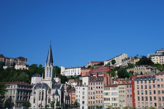 this is a landscape of a few buildings in Lyon, in france, there is many colours and there is a church amoung the buildings. It's situated at the borer of the Rhone. In the  background the blue sky.