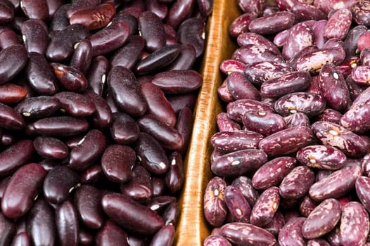 A couple of dark red and spotted kidney beans in wooden dish 