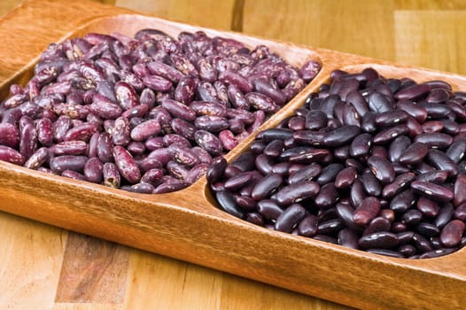 A couple of dark red and spotted kidney beans in wooden dish 