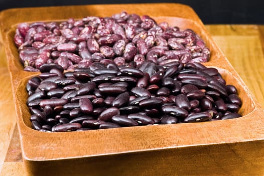 A couple of dark red and spotted kidney beans in wooden dish 