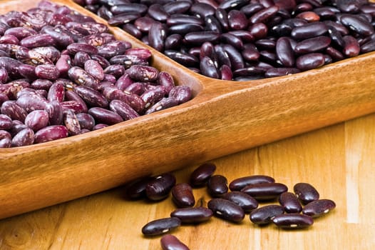 A couple of dark red and spotted kidney beans in wooden dish 