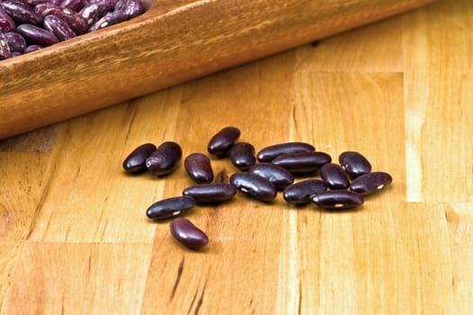 A couple of dark red and spotted kidney beans in wooden dish 