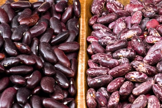 A couple of dark red and spotted kidney beans in wooden dish 