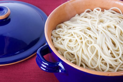 Cooked spaghetti in blue earthenware pot with lid to the side.  