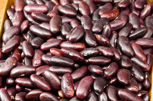 A couple of dark red and spotted kidney beans in wooden dish 