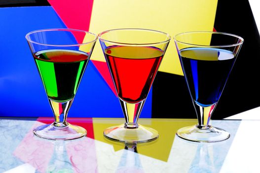 Three transparent glasses with multi-coloured drinks