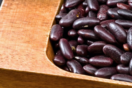 A couple of dark red and spotted kidney beans in wooden dish 