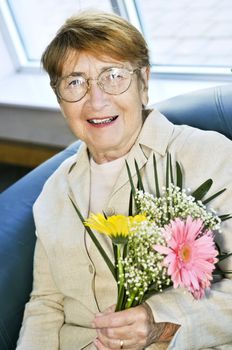 Elderly woman with glasses holding flowers and smiling
