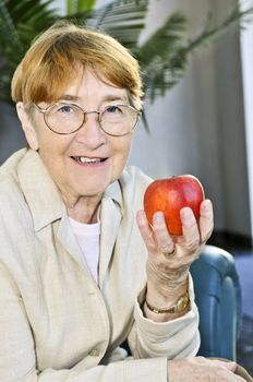 Elderly woman with glasses holding apple and smiling