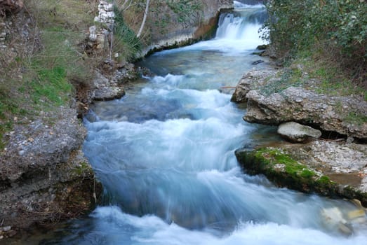 Creek cascade flowing forward with rocks and vegetation on the banks. 