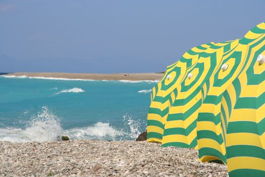 Colorful parasols on a pebble beach with splashing waves in Rhodes, Greece