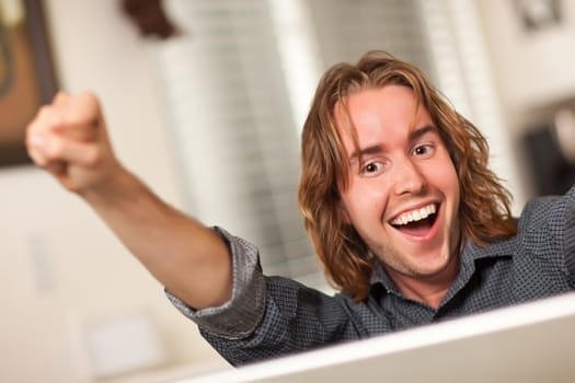 Happy Young Man Using A Laptop Computer and Cheering with Fists in the Air.