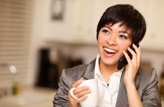 Pretty Smiling Multiethnic Woman with Coffee and Talking on a Cell Phone in Her Kitchen.