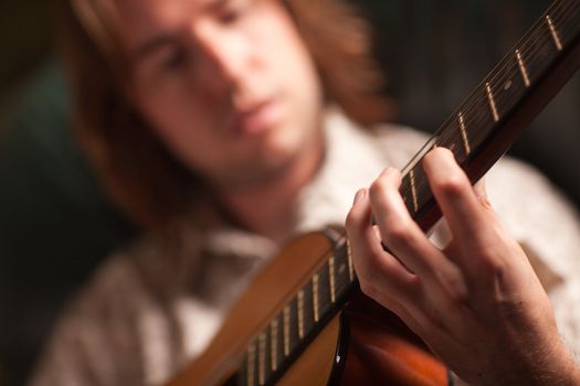 Young Musician Plays His Acoustic Guitar under Dramatic Lighting.