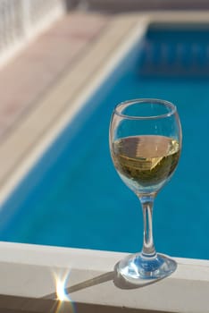 A glass of chilled white wine standing next to a pool