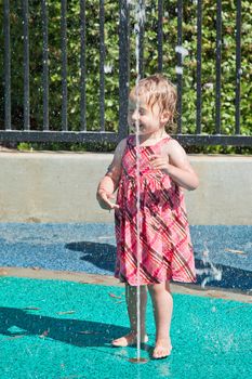 Cute little European toddler girl having fun with water at the playground in park