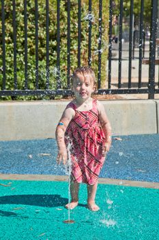 Cute little European toddler girl having fun with water at the playground in park