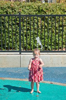 Cute little European toddler girl having fun with water at the playground in park