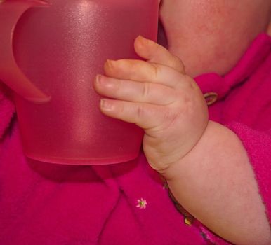 closeup of a babies chubby hands holding a large plastic pink cup