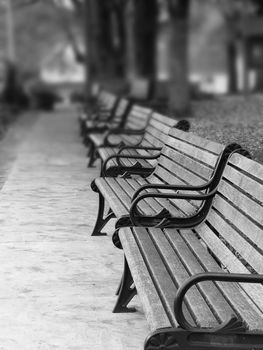 A row of wood and metal benches along a walkway in a park. In black and white with selective blur.