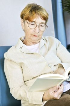 Elderly woman relaxing on couch reading a book