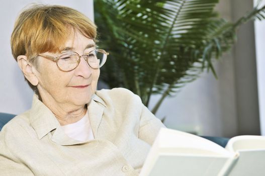 Elderly woman relaxing on couch reading a book
