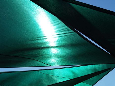 Abstract view of the underside of a green sun shade with sunlight streaming through the fabric.