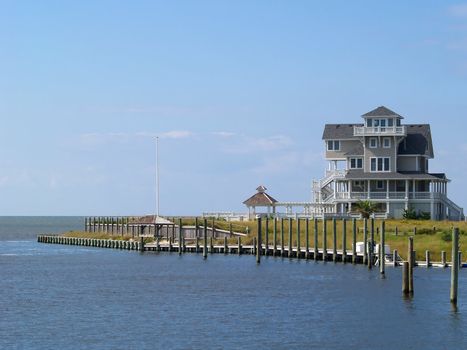 A large vacation home with a tower beside a marina on a large body of water