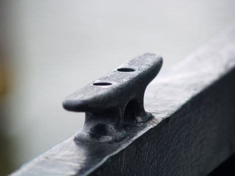 A black painted metal tie-down cleat on the railing of a passenger ferry. Shot with a narrow depth of field with copyspace for text.