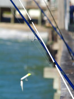 Several fishing rods leaning up against a railing on a weathered fishing pier. 