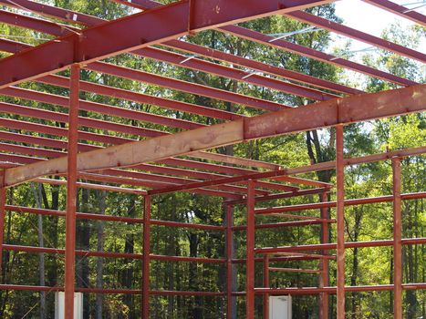 View from inside a new commercial construction project showing girders, beams, bracing and doors against a backdrop of trees.