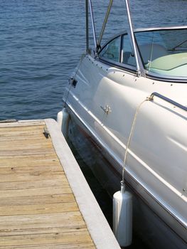 Detail of a sleek speed boat alongside a dock with rubber bumpers, steel railings and a wrap around windshild. Looks like quite a ride!