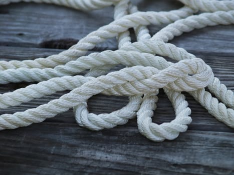 Closeup of a nylon rope laying on a weathered wooden dock. The grain of the wood and the fibers in the rope are quite pronounced. 