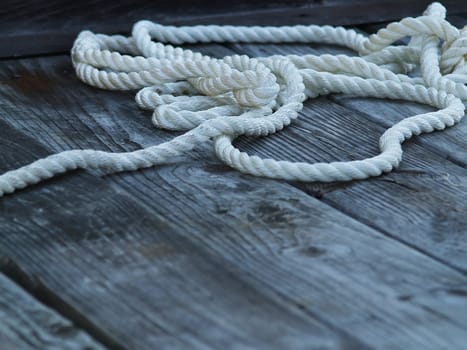 Closeup of a nylon rope laying on a weathered wooden dock with plenty of room for copy space. The grain of the wood and the fibers in the rope are quite pronounced.