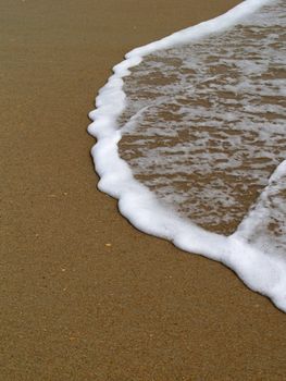 The transition between land and water. The very edge of an ocean wave as it comes to a stop on a sandy beach. 