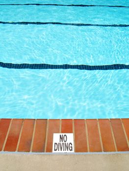 No diving sign embedded in the deck of a community pool, showing the concrete, brick, water and lane markers.