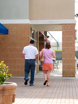 Man and a woman strolling along the brick sidewalk in front of some retail stores