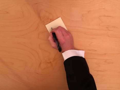 Man writing on a blank sticky note on a wooden desk