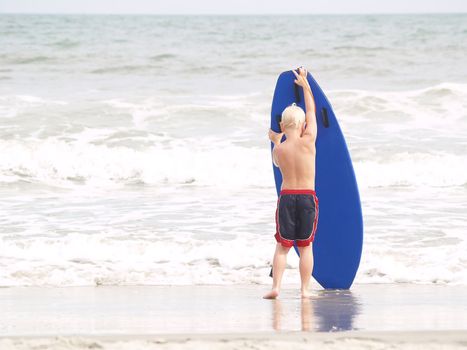Young boy wrestling with a blue surfboard on a bright day