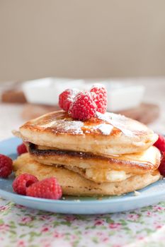 Stack of delicious and fresh american pancakes topped with raspberries and maple syrup