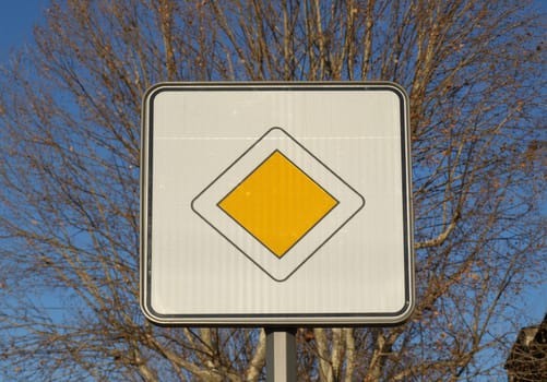 Right of way sign over blue sky with trees