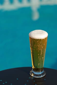 Chilled glass of fresh beer standing next to the pool